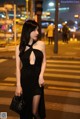 A woman in a black dress standing on a city street at night.