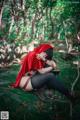 A woman in a red hooded outfit sitting on a rock in the woods.