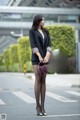 A woman in a black blazer and polka dot tights is standing on the street.