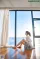 A woman sitting on the floor in front of a large window.