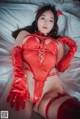 A woman in a red latex outfit laying on a bed.