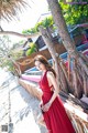 A woman in a red dress standing next to a tree.