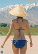 A woman in a bikini and a straw hat walking down a road.