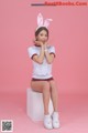 A woman sitting on top of a white cube wearing bunny ears.