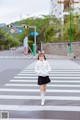 A woman in a white coat and black skirt crossing the street.