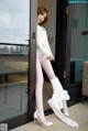 A woman in white stockings and high heels leaning against a glass door.