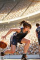 A woman in a basketball uniform dribbling a basketball in front of a crowd.