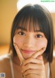 A woman with bangs and a white tank top smiles at the camera.