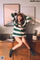 A woman sitting on top of a dresser wearing a green and white striped sweater.