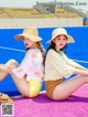 Two young women sitting on a pink and blue tennis court.