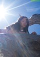 A woman leaning on a tree branch in front of the sun.