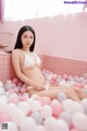 A woman in a white bikini sitting in a bathtub filled with pink and white balloons.